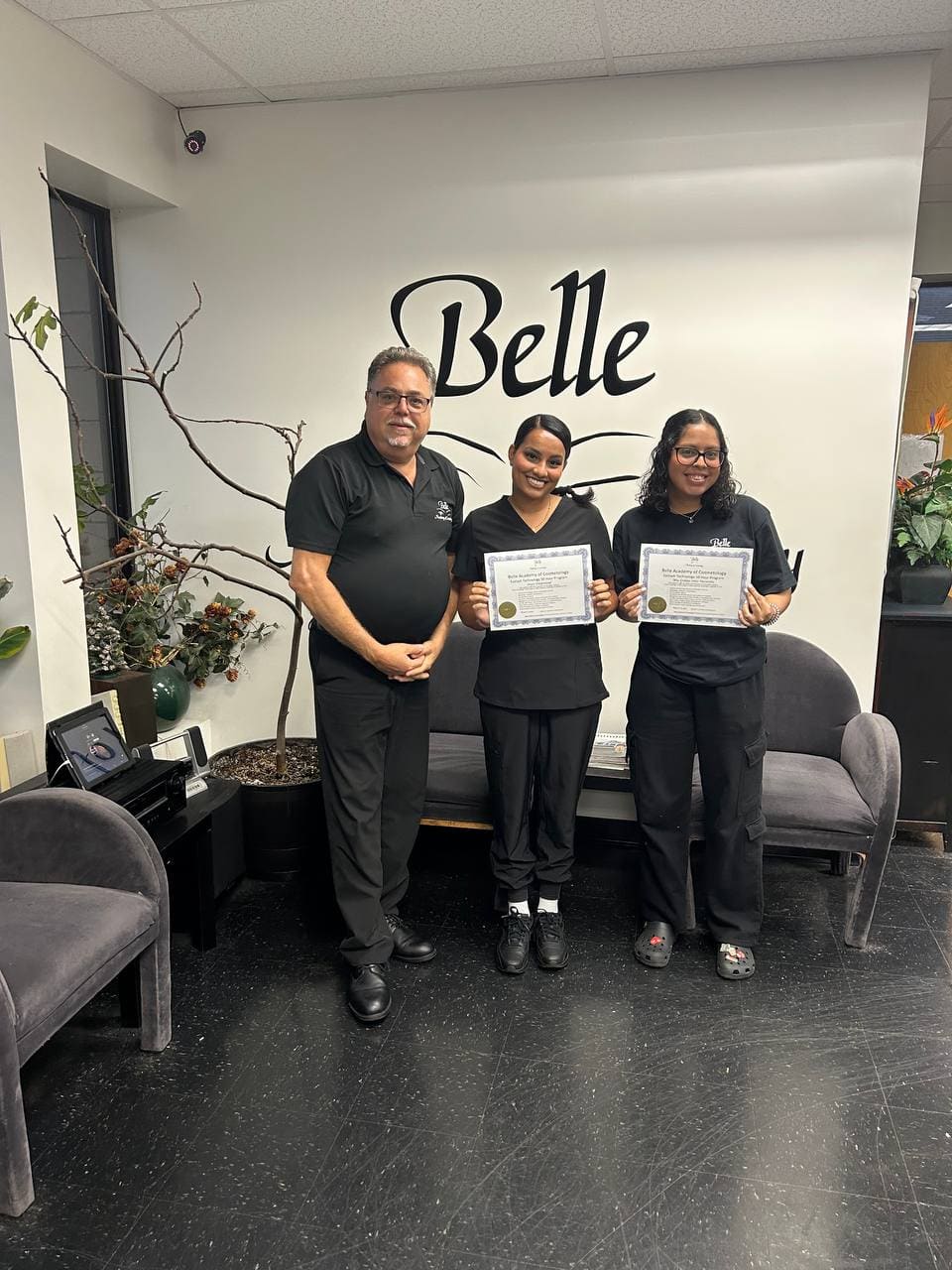 Two Belle Academy graduates with instructor holding certificates